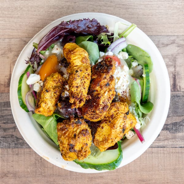 Overhead view of a salad with grilled chicken, mixed greens, cucumbers, red onions, and feta cheese.