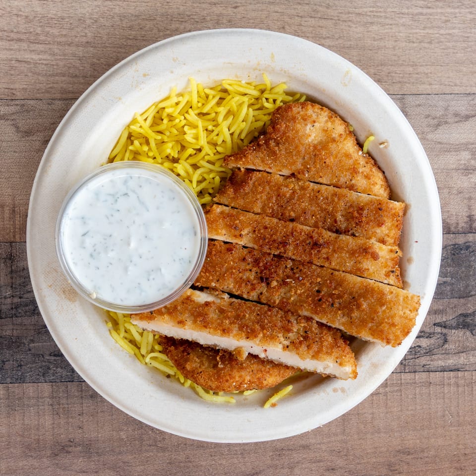 Crispy fried chicken cutlets with yellow rice and a side of white sauce in a paper bowl.