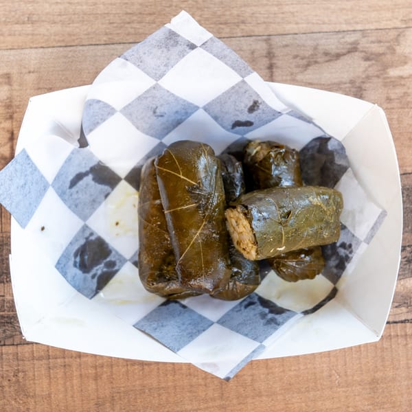 Several dolmades, or stuffed grape leaves, in a white paper tray with checkered lining.
