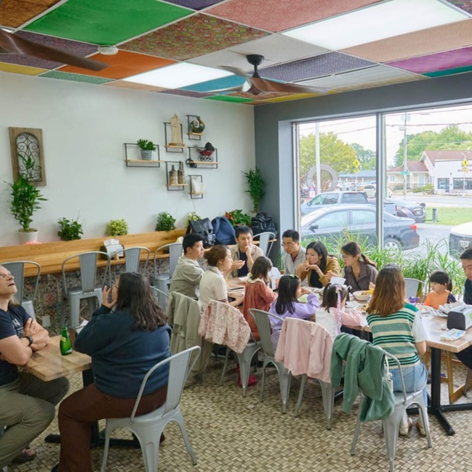 Diverse group of people, including families with children, dining at tables in a brightly lit restaurant.