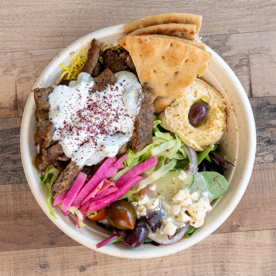 A gyro bowl with meat, rice, hummus, pita bread, salad, and pickled vegetables.