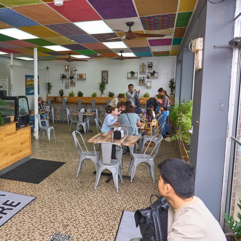 Restaurant interior with patrons seated at tables, colorful ceiling tiles, and plants along the wall.