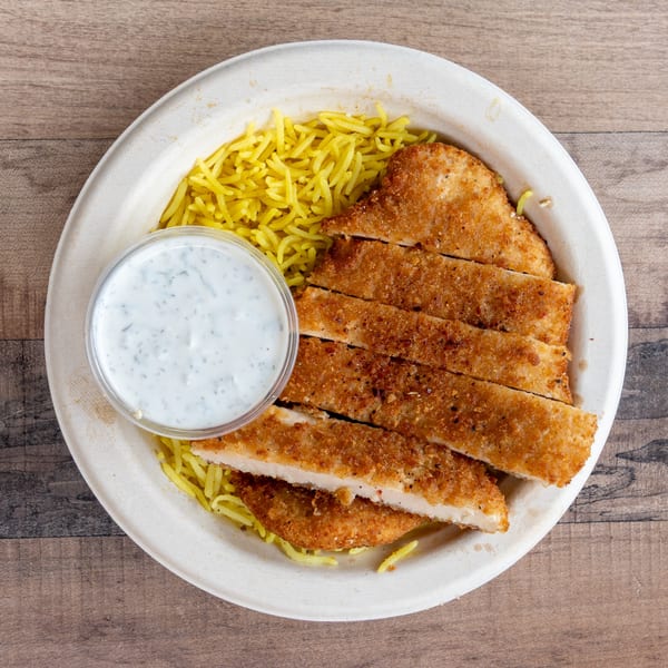 Crispy fried chicken cutlets with yellow rice and a side of white sauce in a bowl.
