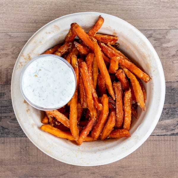 Sweet potato fries in a white bowl with a side of ranch dressing on a wooden table.
